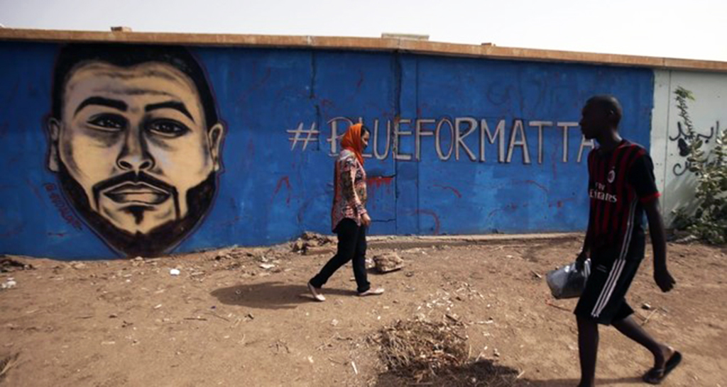 Sudanese artist Asil Diab (L), walks in front of a mural painting of Mohamed Mattar, on the wall of a youth club in Bahri in Khartoum, July 21. Mattar was among dozens killed in the June 3 raid on a protest camp outside the military headquarters.